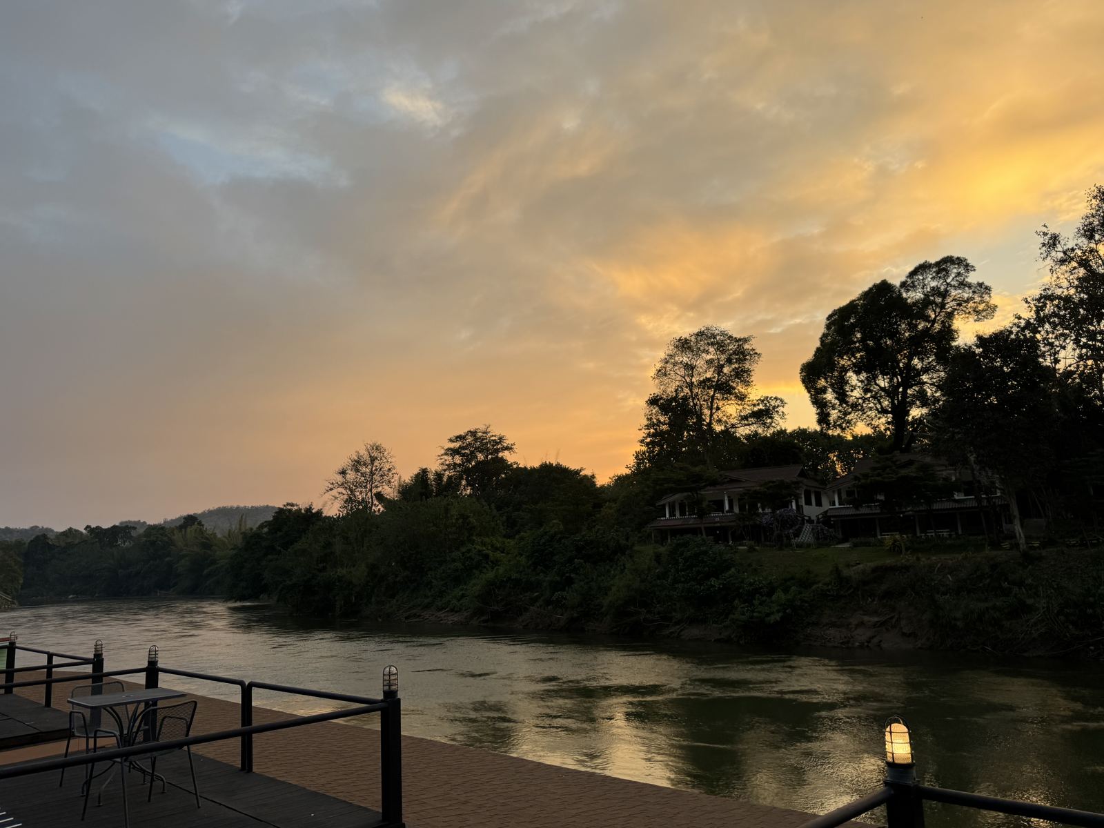 Dusk over the River Kwai seen from the deck of a raft house, trees silhouetted on the far bank