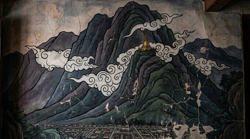 A cracked temple mural of a golden stupa high on a mist-wrapped mountain above a gridded city